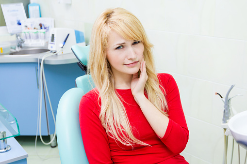 Blonde in dental chair holding jaw at  St. Louis Prosthodontics in St. Louis, MO